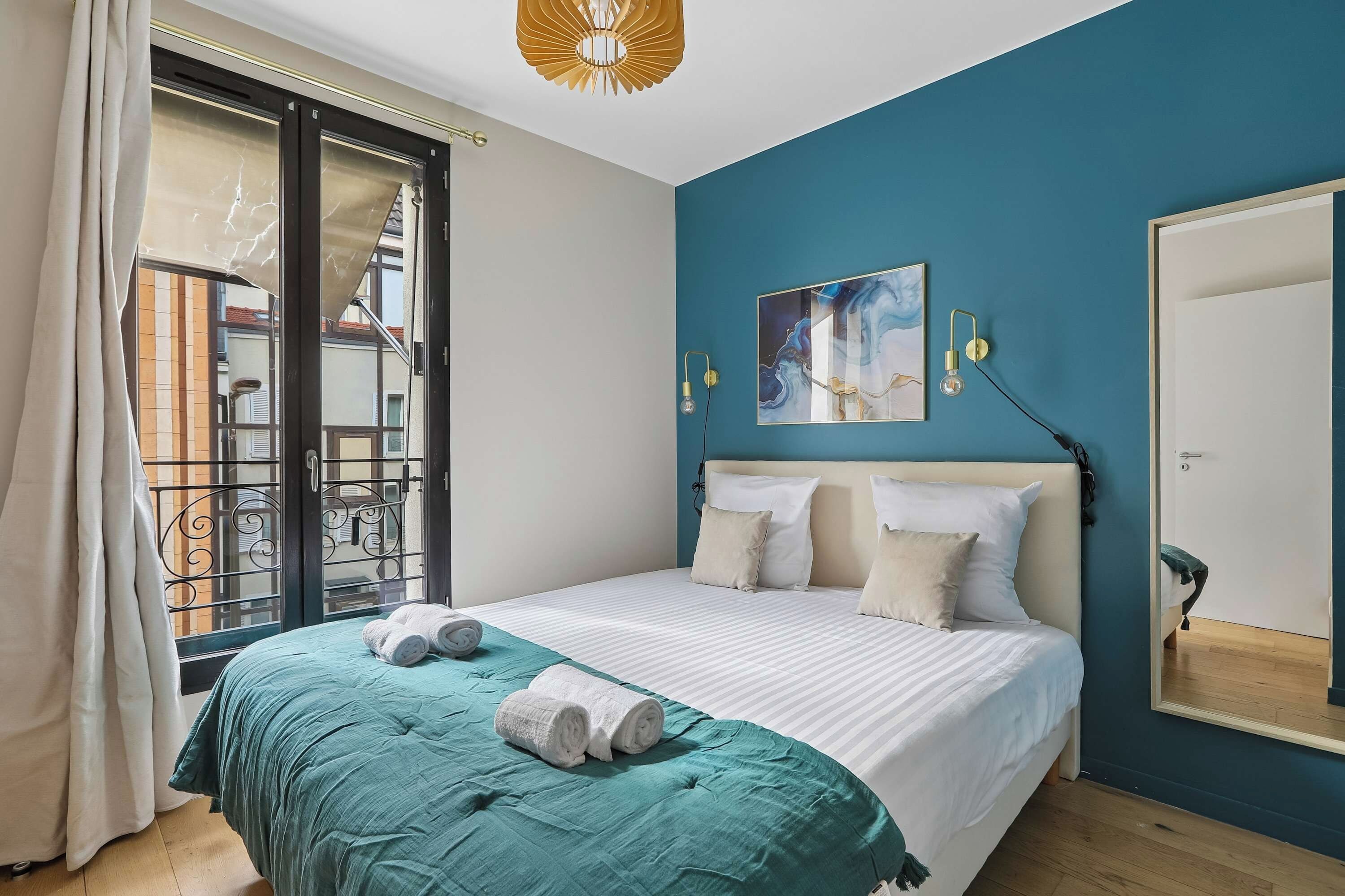 Ein Schlafzimmer mit einem Bett, einem großen Fenster, einem Gemälde und einem Spiegel.