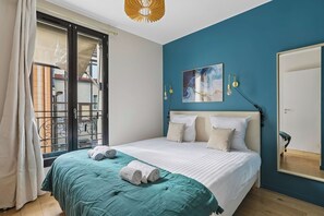 A bedroom with a bed, a large window, a painting, and a mirror. - Modern Apartment in Boulogne-Billancourt (Boulogne-Billancourt)