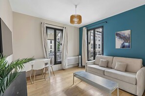 A modern living room with a sofa, a dining table with chairs, and a large window with curtains. - Modern Apartment in Boulogne-Billancourt (Boulogne-Billancourt)