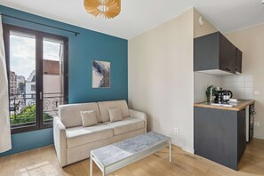 Un apartament modern amb un sofà, una banca, una cuina i un balcó.