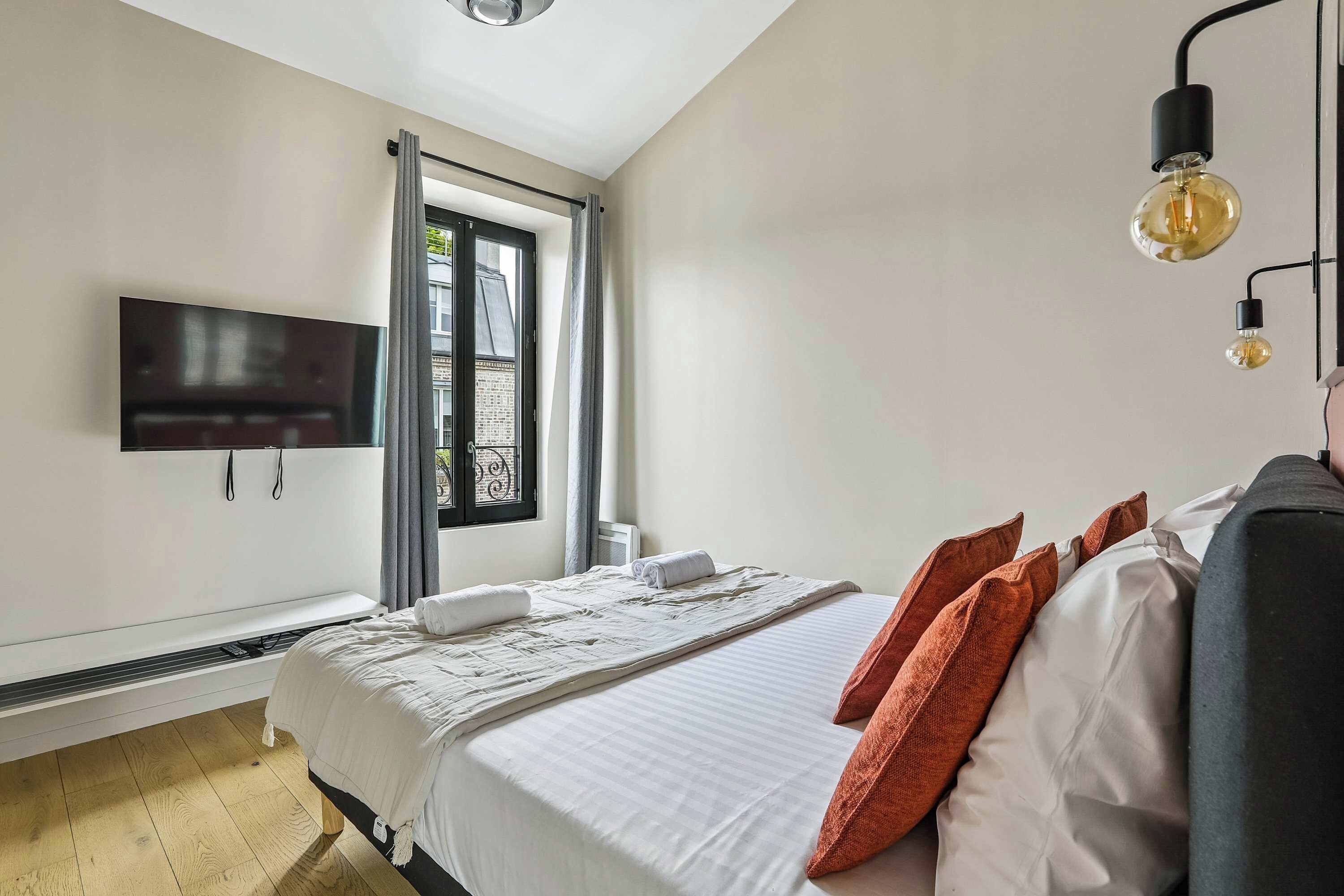 A bedroom with a bed, pillows, a TV, and a window.
