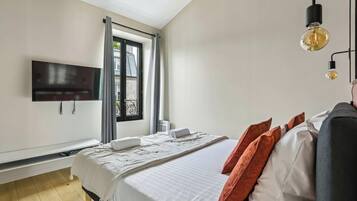 A bedroom with a bed, pillows, a TV, and a window.
