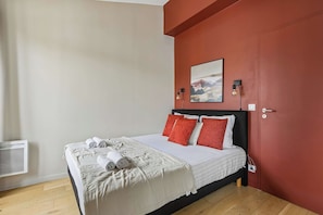 A bedroom with a bed, pillows, a blanket, a wall-mounted picture, and a light fixture. - Cozy Apartment with Kitchen & Sofa Bed (Boulogne-Billancourt)