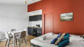 A modern bedroom with a bed, pillows, a desk, and a kitchenette.