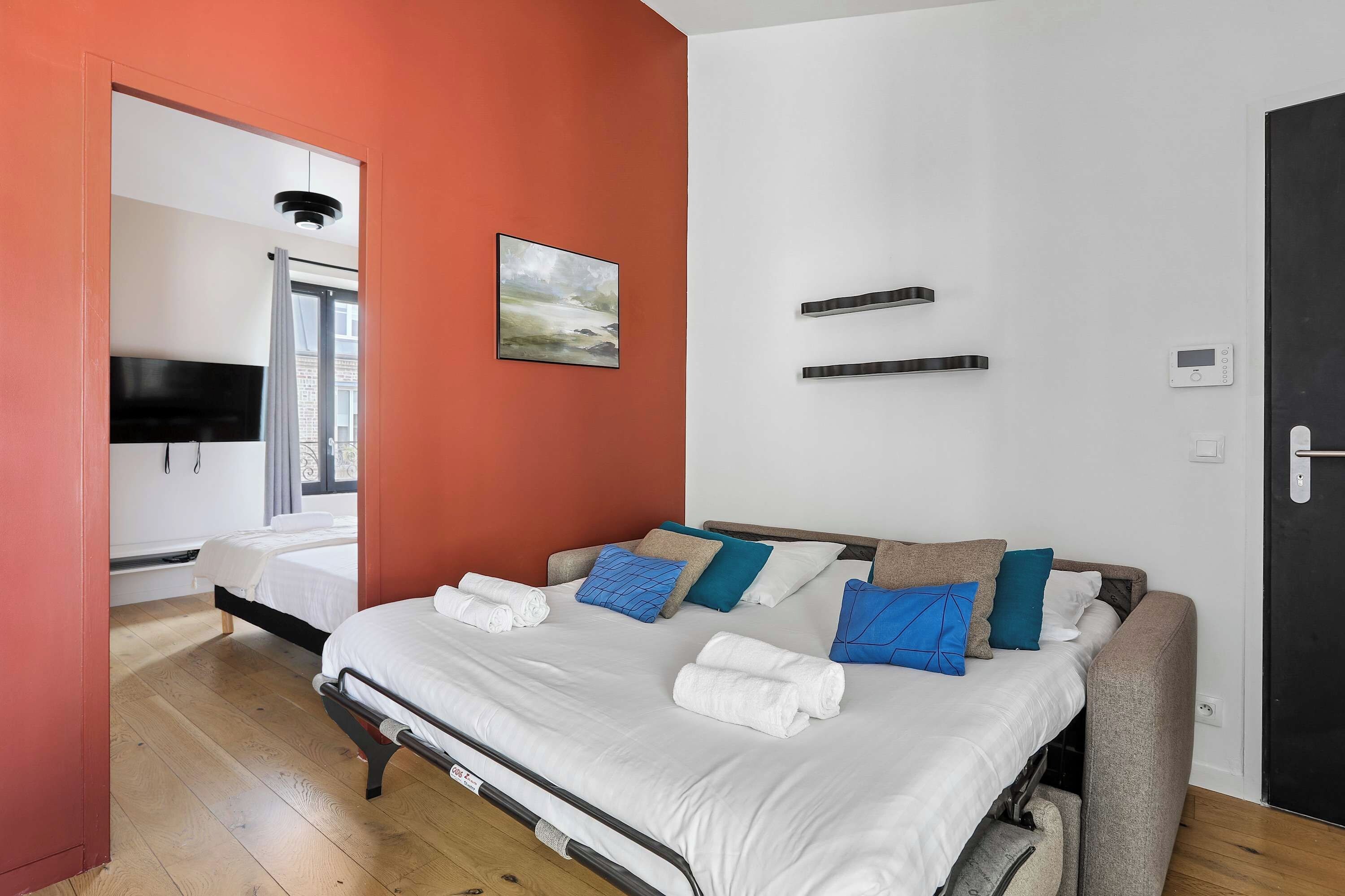 A hotel room with a bed, a TV, a painting, and a door.