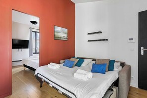 A hotel room with a bed, a TV, a painting, and a door. - Cozy Apartment with Kitchen & Sofa Bed (Boulogne-Billancourt)