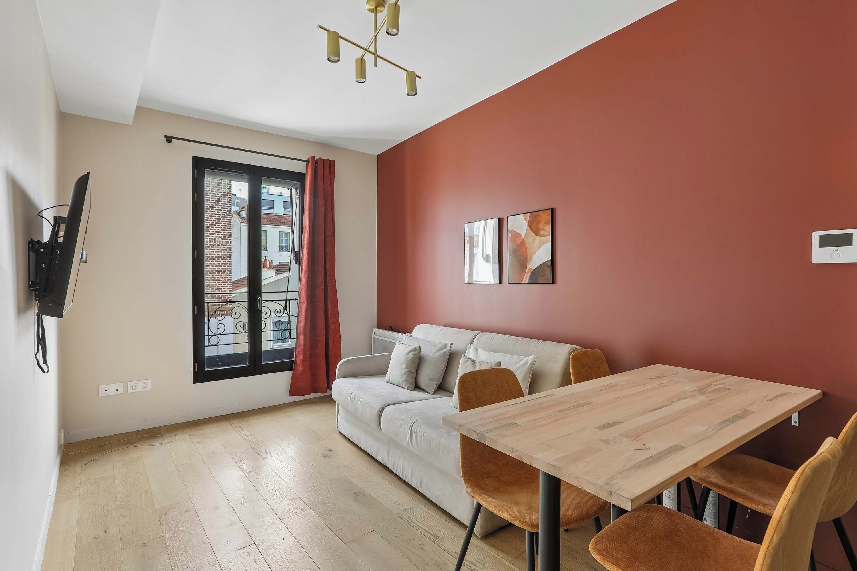 A modern living room with a sofa, a dining table, and a red accent wall.