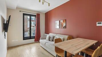 A modern living room with a sofa, a dining table, and a red accent wall.
