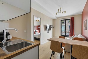 A modern kitchen with a stainless steel sink and a dining area with a wooden table and chairs. - Stylish Apartment with Cozy Bedroom & Sofa Bed (Boulogne-Billancourt)
