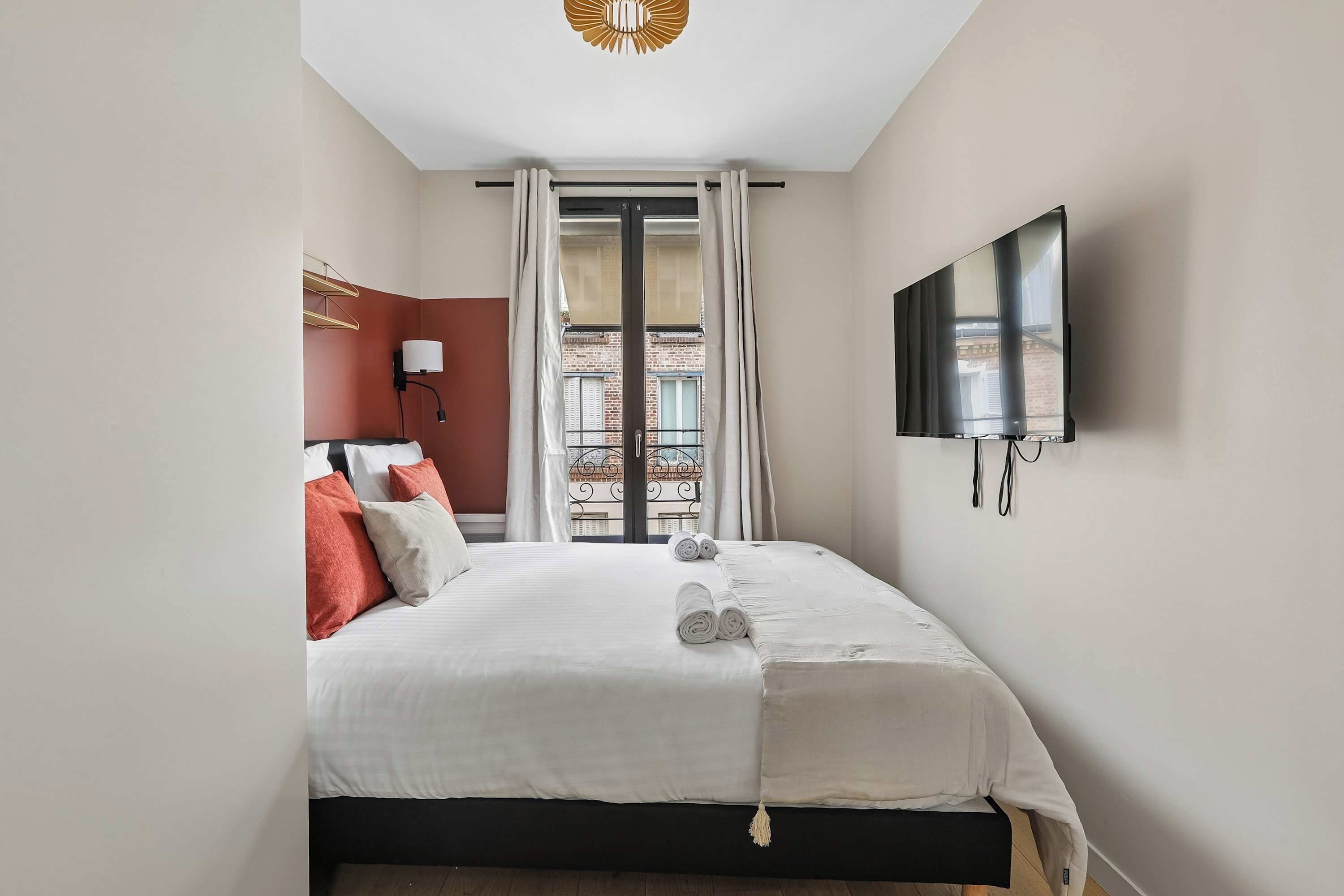 A hotel room with a bed, a TV, and a view of the outside.