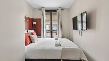 A hotel room with a bed, a TV, and a view of the outside.