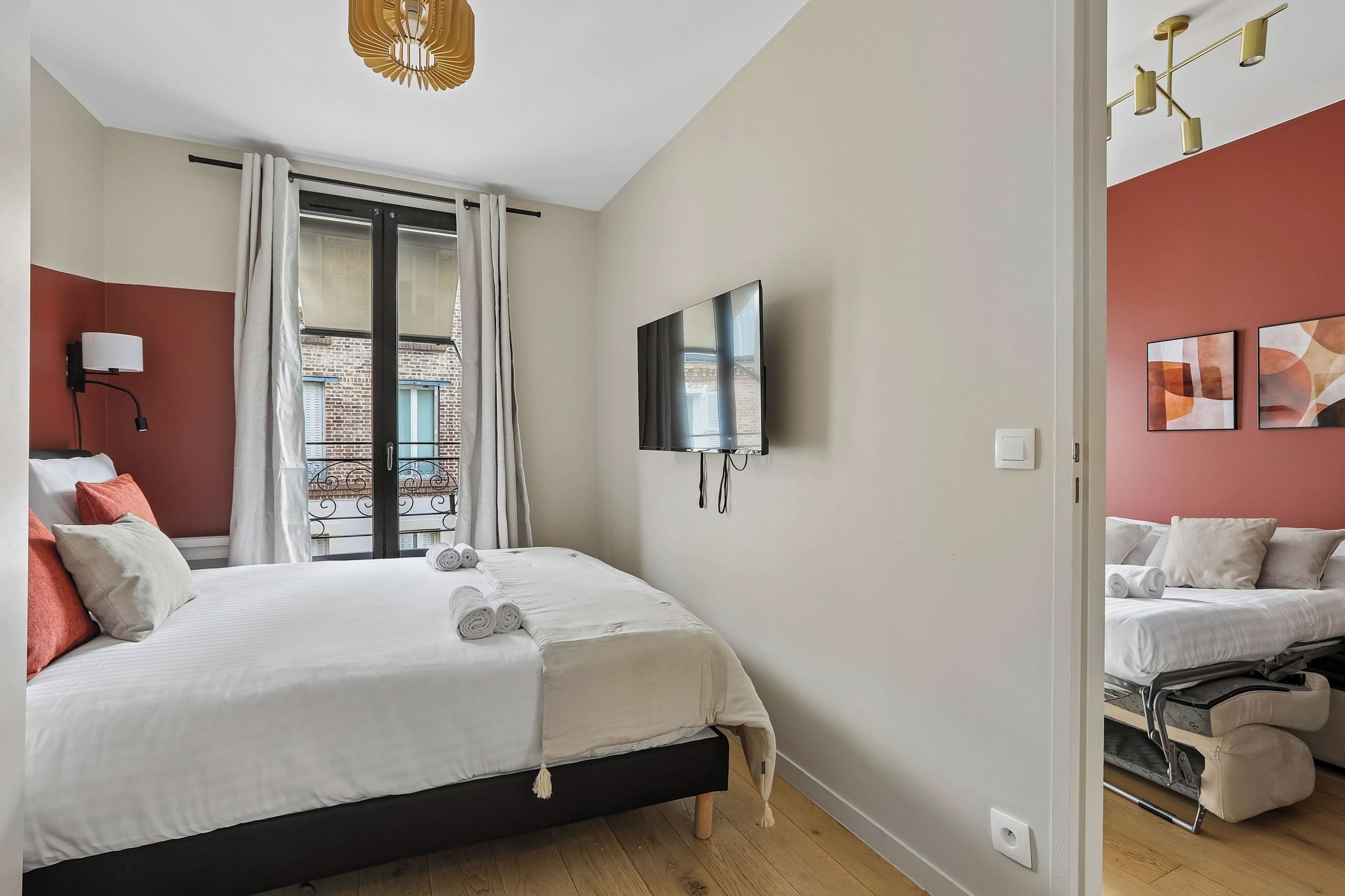Habitación de hotel con cama, televisión, ventana con cortinas, lámpara de pared y obras de arte.