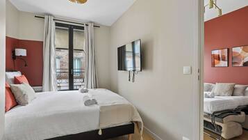 Habitación de hotel con cama, televisión, ventana con cortinas, lámpara de pared y obras de arte.