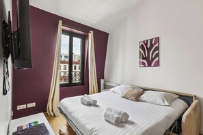 A hotel room with a bed, a window with curtains, a mounted TV, and a wall-mounted artwork. - Cozy Apartment in Boulogne-Billancourt (Boulogne-Billancourt)