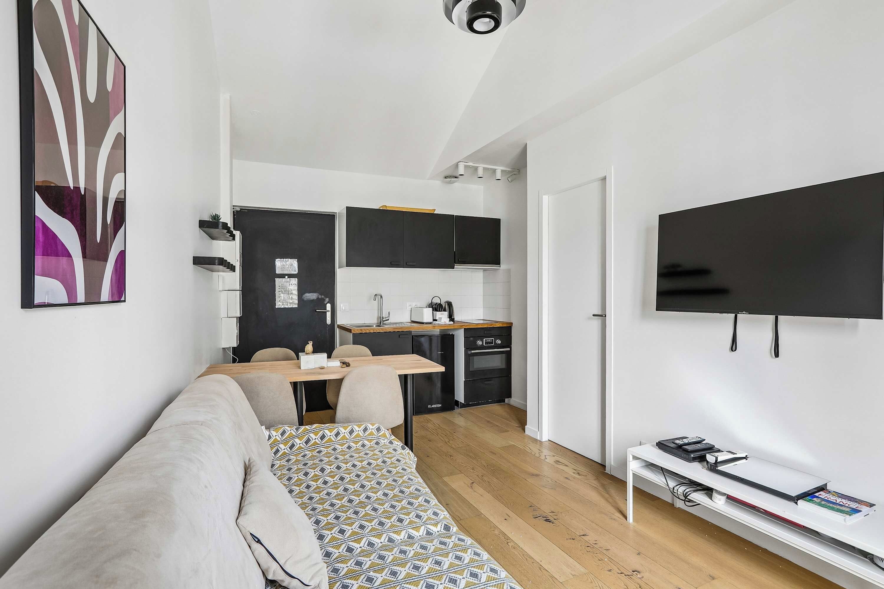 Un espace de vie compact comprenant un coin cuisine, un canapé, une télévision et une petite table à manger.