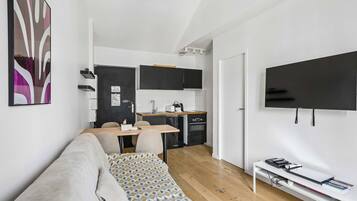 Un espacio habitable compacto con kitchenette, un sofá, un televisor y una pequeña mesa de comedor.