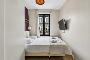 A bedroom with a bed, a TV mounted on the wall, and a window with a view of buildings. - Cozy Apartment in Boulogne-Billancourt (Boulogne-Billancourt)