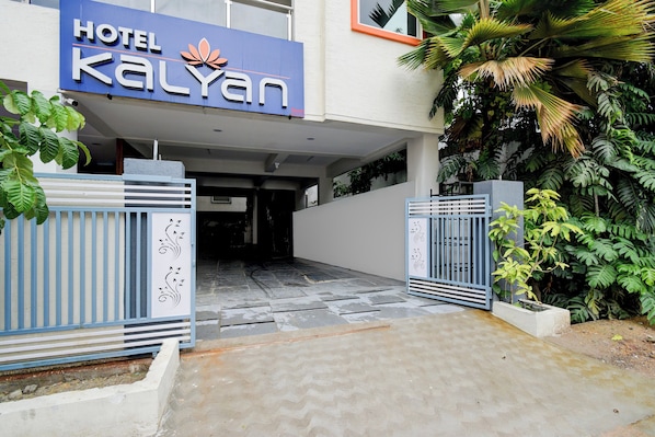 Entrada de hotel con un letrero que dice 'HOTEL KALYAN', un camino de acceso con puerta y follaje circundante.