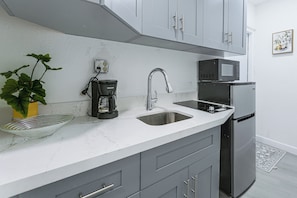 A modern kitchen with grey cabinets, a stainless steel sink, a coffee maker, a microwave, and a refrigerator.