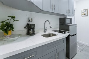 Una cocina moderna con armarios grises, un lavamanos de acero inoxidable, una cafetera, un microondas y un refrigerador.