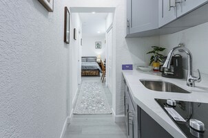 A narrow hallway leading to a bedroom with a bed, a bedside table, and a lamp.