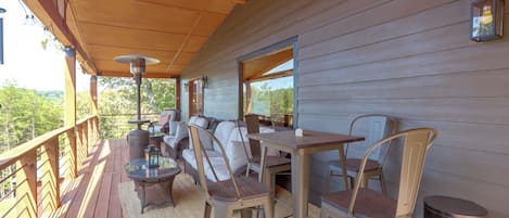 An outdoor patio with a wooden deck, metal chairs, a table, and a built-in sofa.