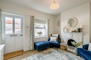 A room with a fireplace, a blue sofa, a patterned rug, and a window with curtains. - Host Stay Silk Weaver s Cottage (Norwich)