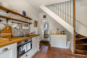 A kitchen with wooden shelves, a stove, and a tiled backsplash. - Host Stay Silk Weaver s Cottage (Norwich)