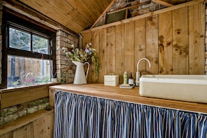 A rustic kitchen with wooden walls, a window with a view, a sink, and a vase with flowers on the counter. - Host Stay Silk Weaver s Cottage (Norwich)