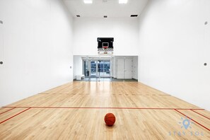 Un vaste terrain de basket-ball intérieur doté d’un plancher en bois, d’un panier de basket et offrant une vue dégagée sur l’extérieur grâce à des portes vitrées.
