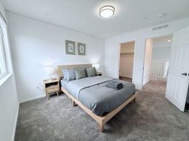 Un dormitorio con cama, mesitas de noche, armario y una puerta que da a otra habitación.