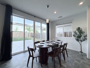 A dining area with a round table set for six, surrounded by chairs, with a view of a backyard through large sliding glass doors. - Luxury 5B 3B Near Casino Ac Prking Greatneighbors (Elk Grove)