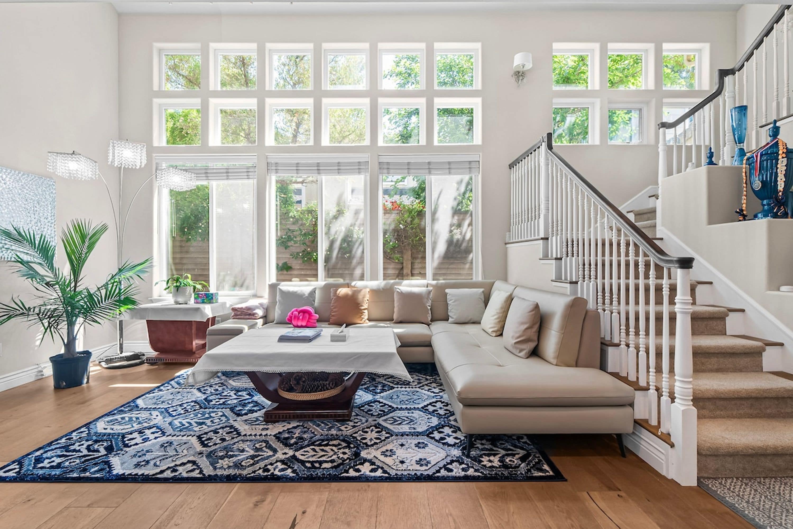 Un salon spacieux avec une grande fenêtre, un escalier et un tapis à motifs bleus.