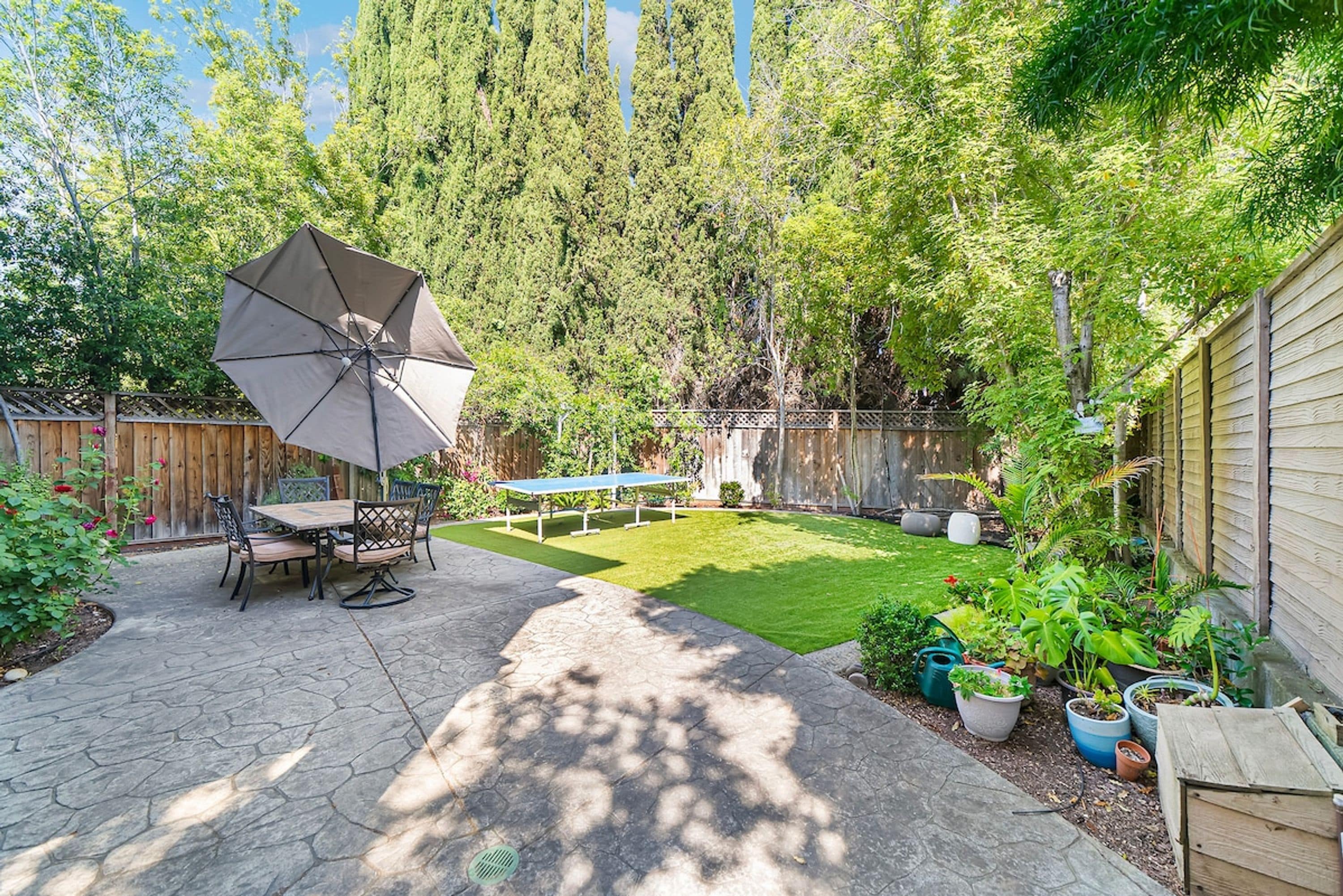 A backyard with a patio table and chairs, a lawn, and a wooden fence.