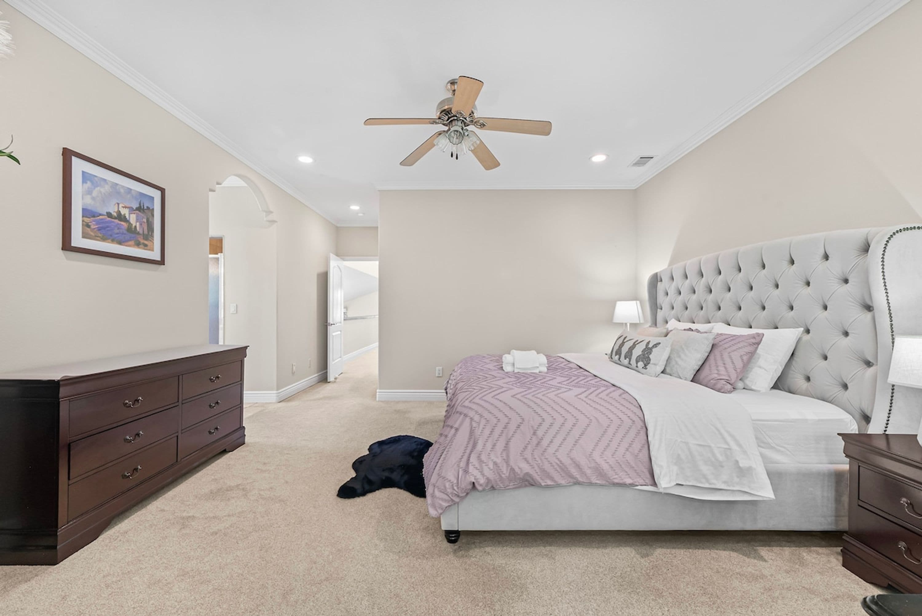 A bedroom with a bed, a dresser, a ceiling fan, and a painting on the wall.