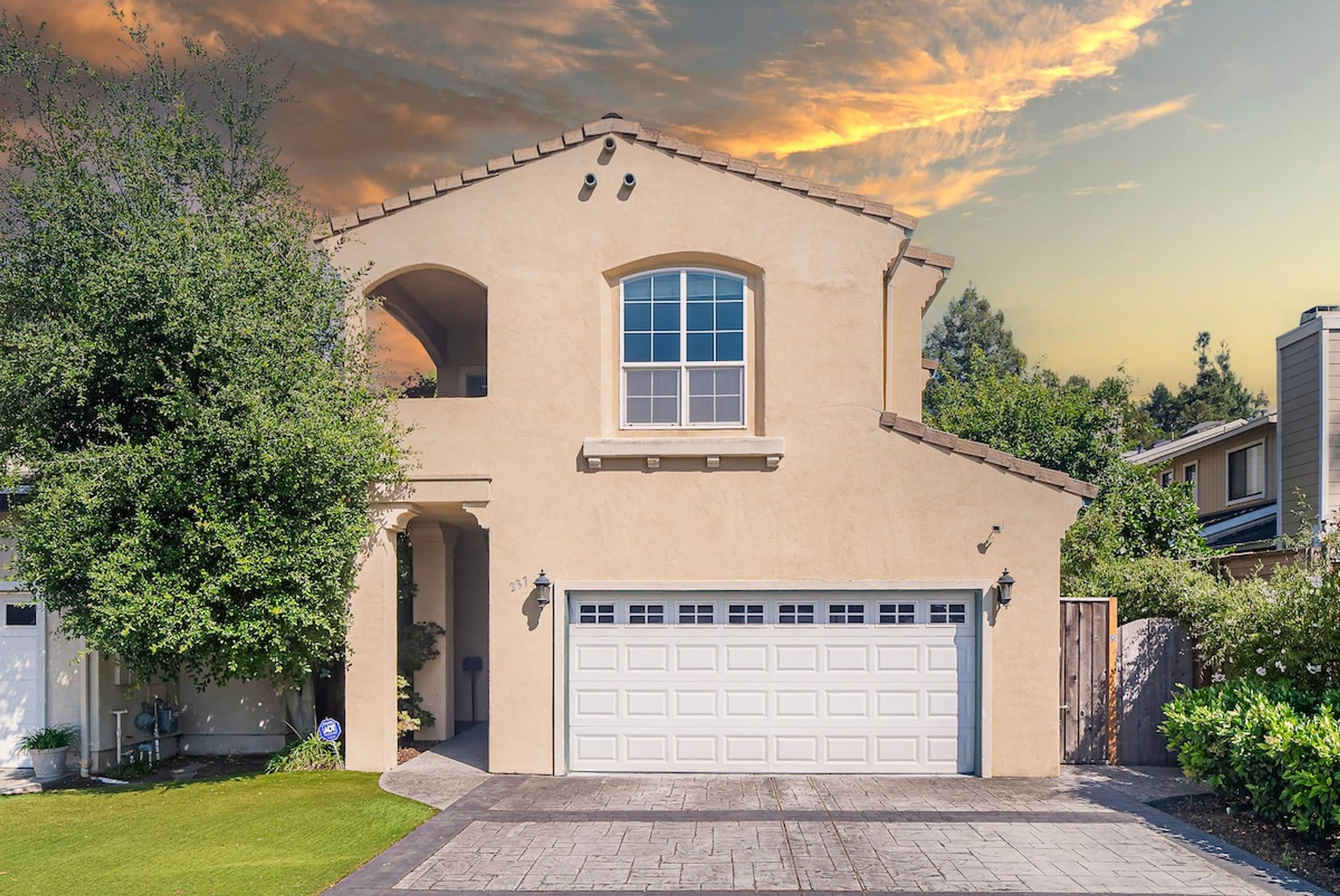 A two-story house with a garage, a large arched window, and a flat roof.