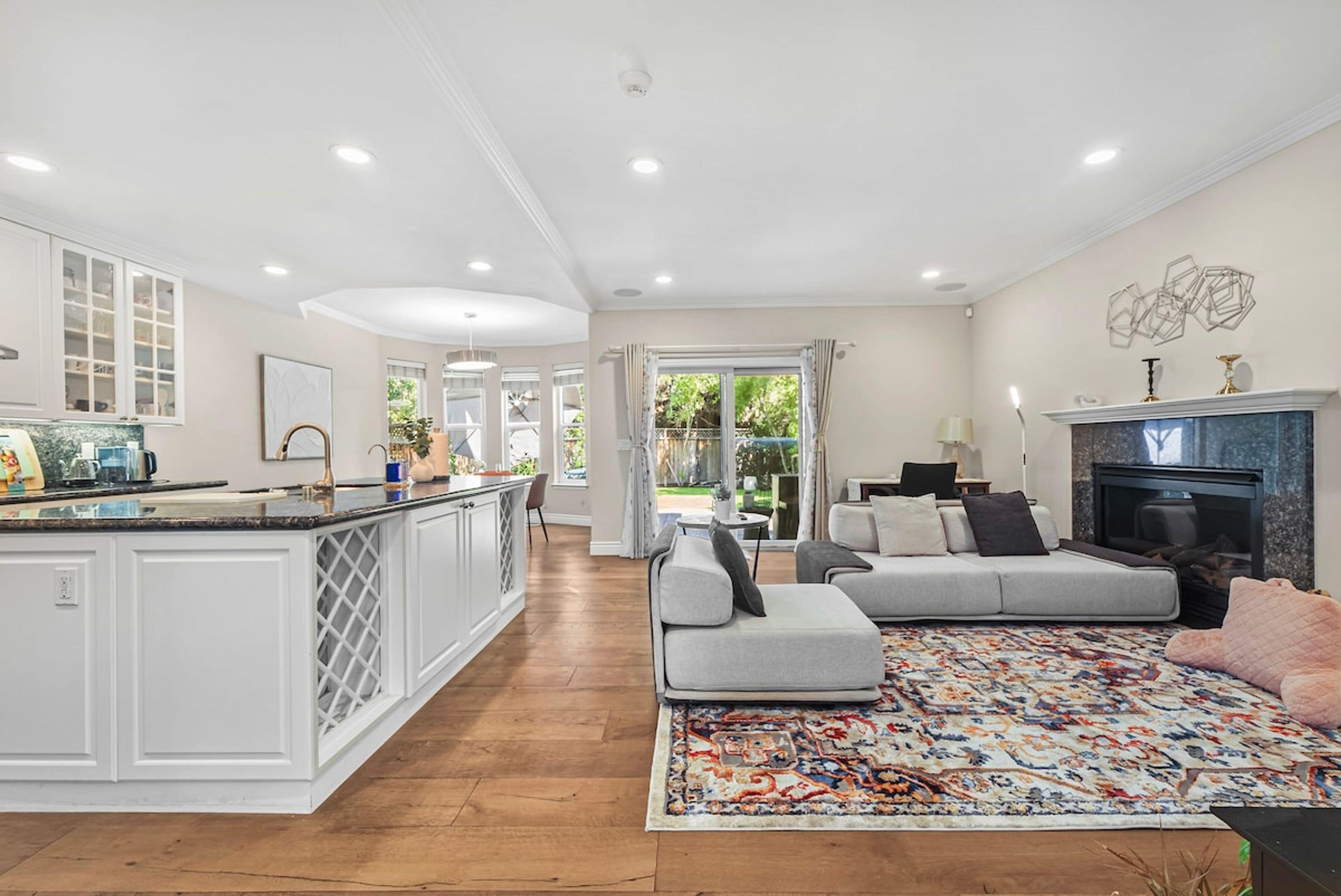 A spacious living area with a large sofa, a fireplace, and a kitchen with white cabinetry.