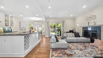 A spacious living area with a large sofa, a fireplace, and a kitchen with white cabinetry.