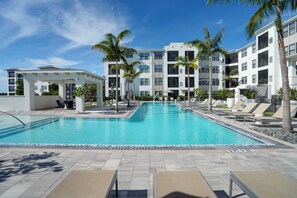 A swimming pool with lounge chairs and palm trees, surrounded by multi-story buildings. - 2BR Coastal Condo in Bradenton 3 Mi to IMG (Bradenton)