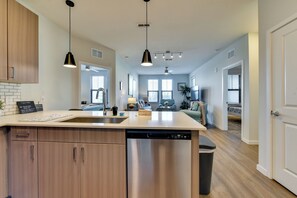 Een moderne keuken met een centraal eiland, roestvrijstalen apparatuur, hanglampen en uitzicht op de woonkamer.