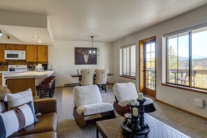 A spacious living area with a kitchen in the background, a dining table with chairs, and large windows offering a view of the outdoors. - Hikes + Hot Tub Soaks! Extended Silverthorne Stay (Silverthorne)
