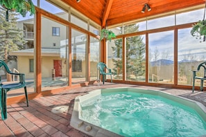 A covered outdoor area with a hot tub, brick flooring, and large windows offering a view of a residential area. - Hikes + Hot Tub Soaks! Extended Silverthorne Stay (Silverthorne)