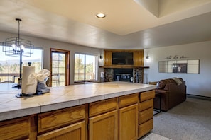 A spacious kitchen with a large island, wooden cabinets, and a stone fireplace. - Hikes + Hot Tub Soaks! Extended Silverthorne Stay (Silverthorne)