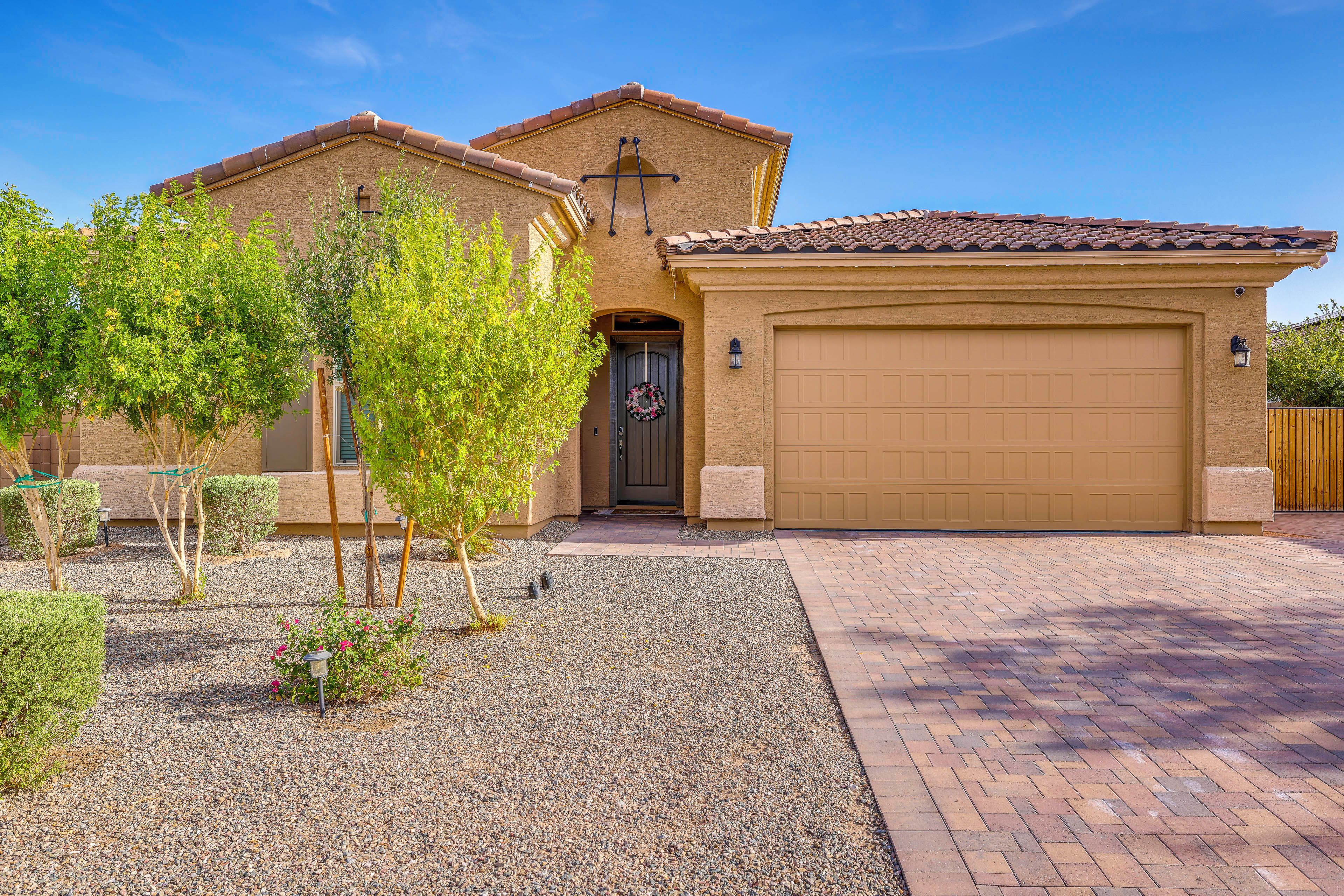 A two-story house with a garage, gravel driveway, and a small garden with trees and shrubs.