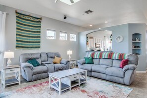 A living room with two grey sofas, a white coffee table, and a colorful rug. There are two side tables with lamps, a large window with blinds, and a kitchen visible through an archway. - Desert Oasis: Tucson Home w/ Private Swim Spa (Tucson)
