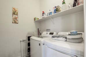 A laundry room with a front-loading washer and dryer, a radiator, and a shelf with cleaning supplies. - Desert Oasis: Tucson Home w/ Private Swim Spa (Tucson)