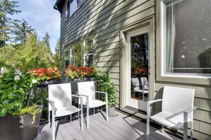 A wooden deck with two white chairs and a table, surrounded by potted plants and flowers.