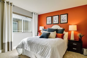 A bedroom with a large bed, two bedside tables, a window with curtains, and three framed pictures on the wall.