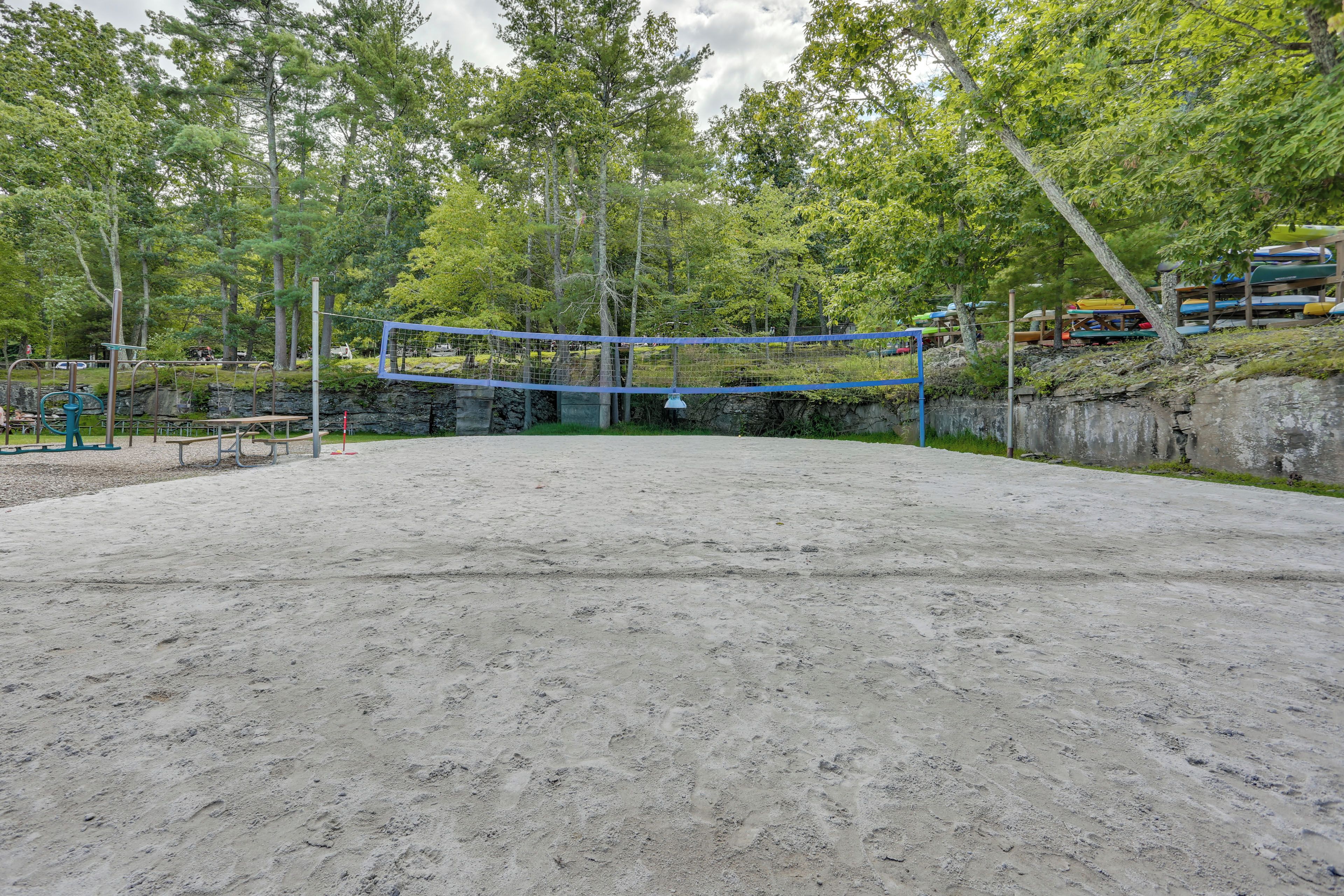 Een buitenvolleybalveld met een net, omgeven door bomen en een rotsachtig gebied.