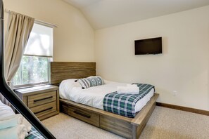 Ein Schlafzimmer mit einem Bett, einem Fernseher, einem Fenster mit Vorhängen und einem Schreibtisch mit Schubladen.